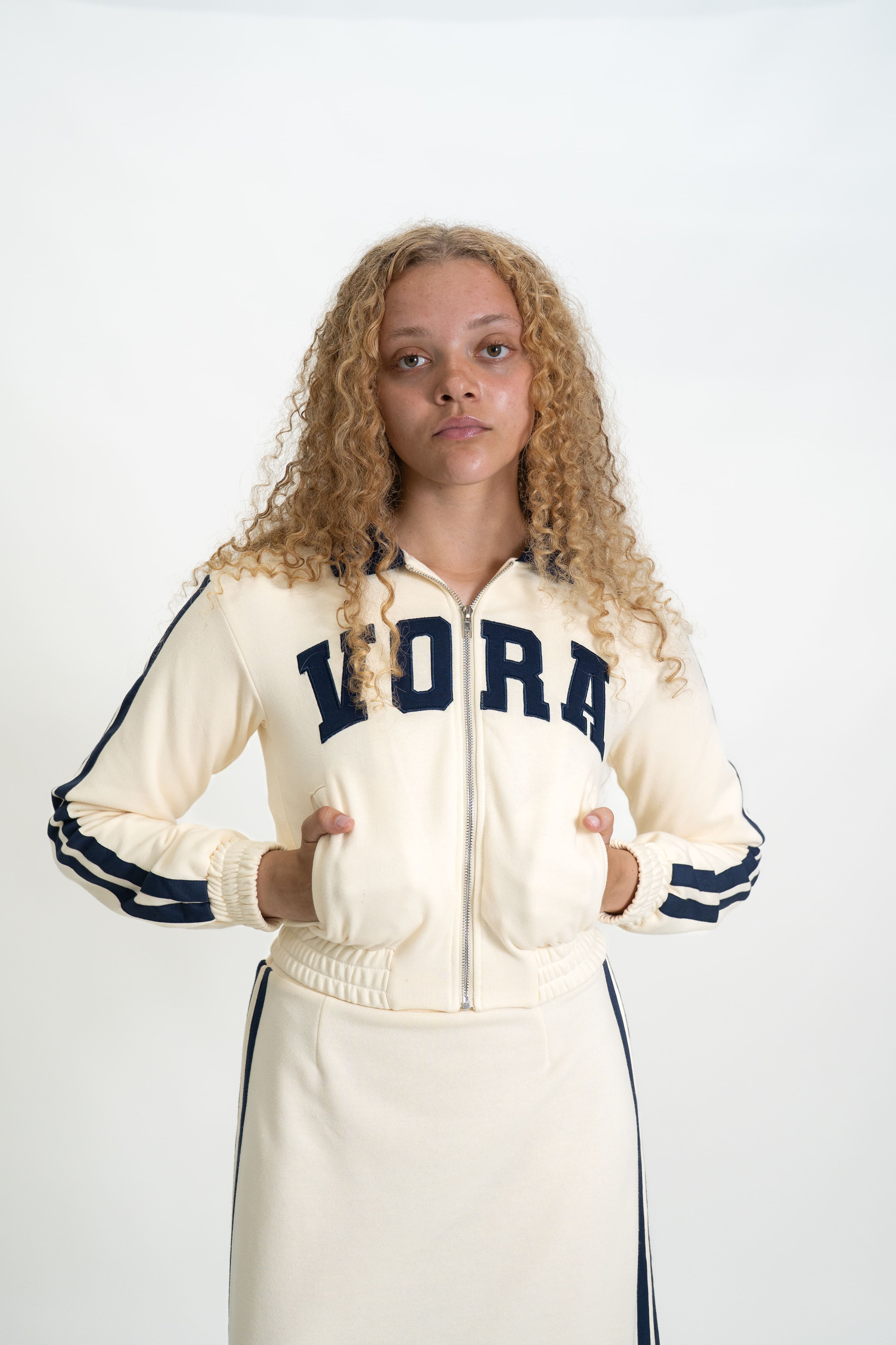 Woman wearing a cream-colored tracksuit with 'VORA' branding on a white background
