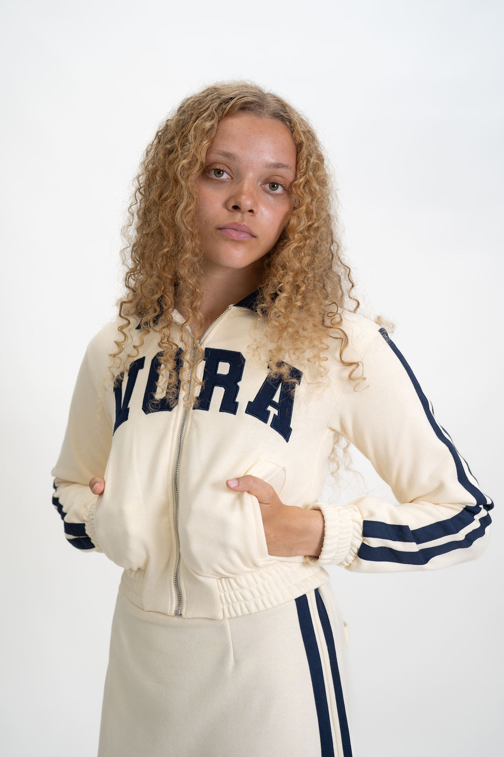 Woman wearing a cream tracksuit with 'Vora' branding on a white background