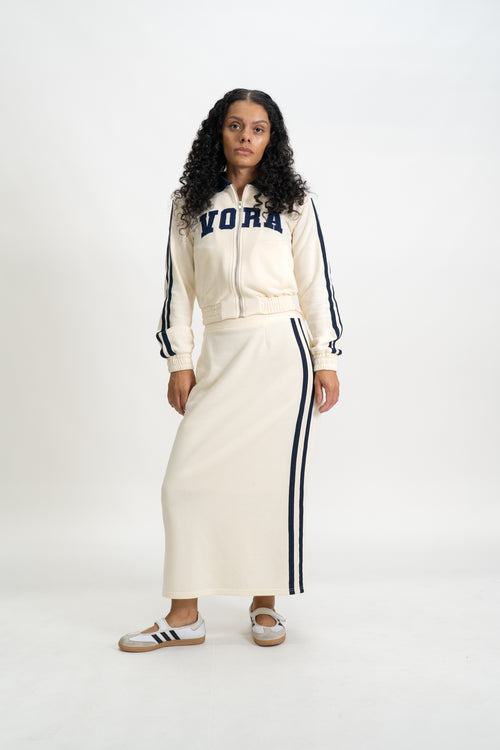 Person wearing a cream-colored tracksuit with 'VORA' text on a white background